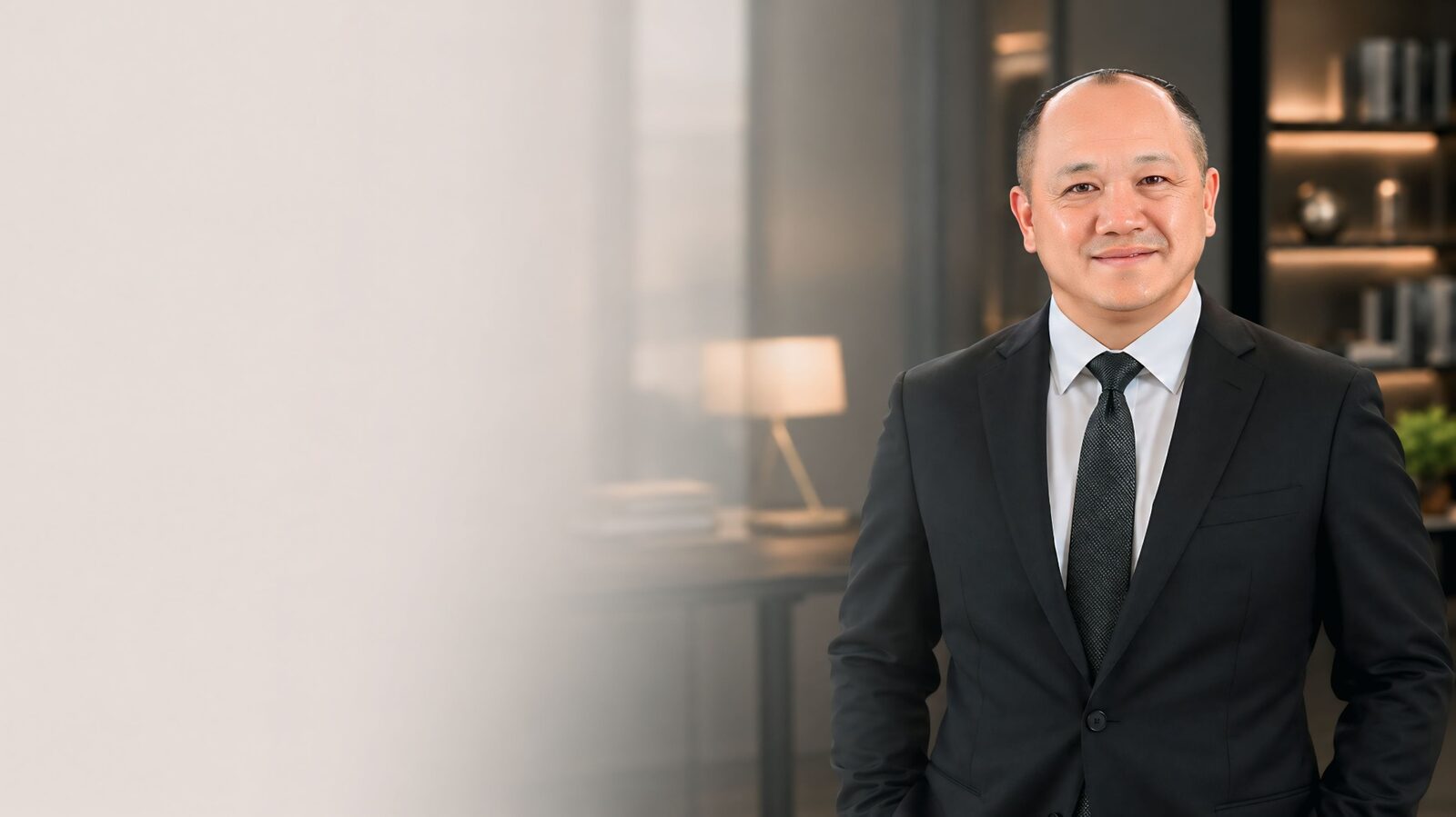 Portrait of Visual Xiong, independent licensed insurance agent with Freedom Equity Group, in a tailored navy suit standing in a warm modern office.